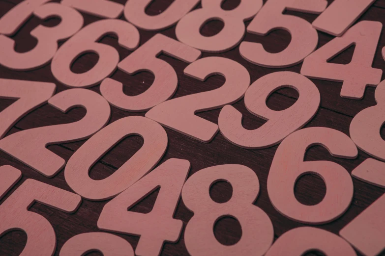 a pile of numbers sitting on top of a wooden table, dull pink background, ffffound, 9 9 designs, medium close up