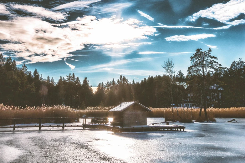 a boathouse sitting on top of a frozen lake, by Jesper Knudsen, pexels contest winner, hurufiyya, sunny day in the forrest, early evening, bright sky, wide - angle view