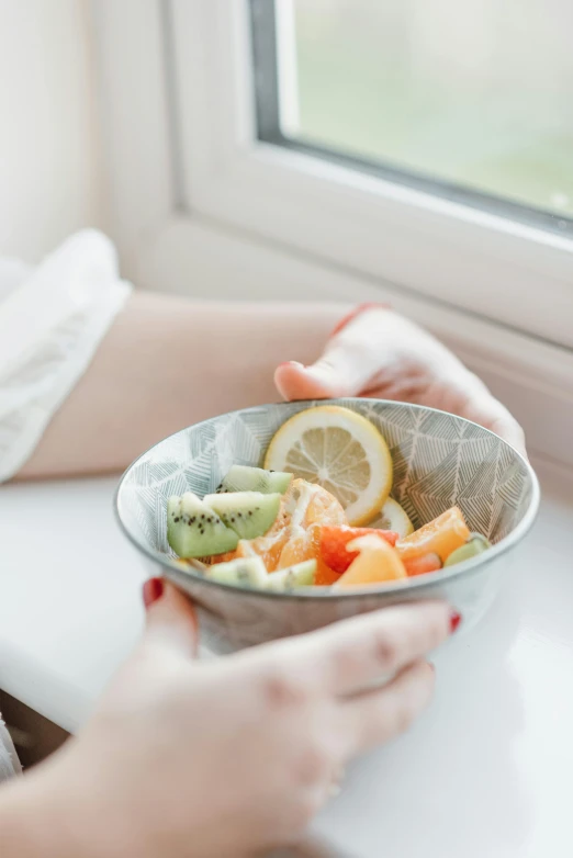 a close up of a person holding a bowl of food, a still life, fresh fruit, natural light window, 🐿🍸🍋, grey