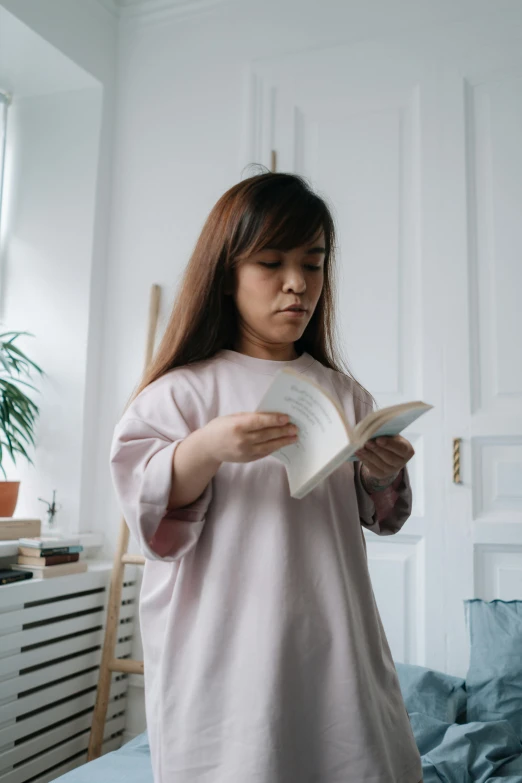 a woman reading a book while standing on a bed, inspired by Kim Jeong-hui, pexels contest winner, wearing a light shirt, wearing a pink dress, dressed as an oracle, wearing casual clothing