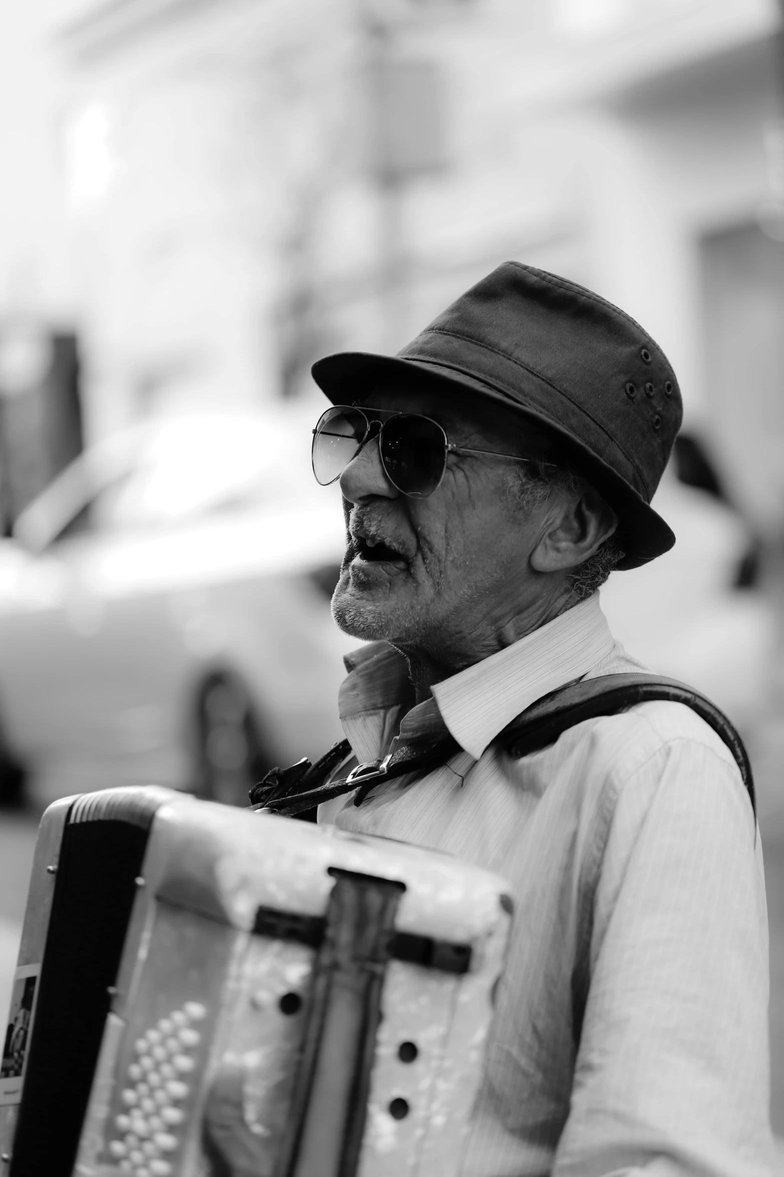 an old man is playing an accordion on the street, a black and white photo, pexels contest winner, wearing sunglasses and a hat, square face, 15081959 21121991 01012000 4k, australian