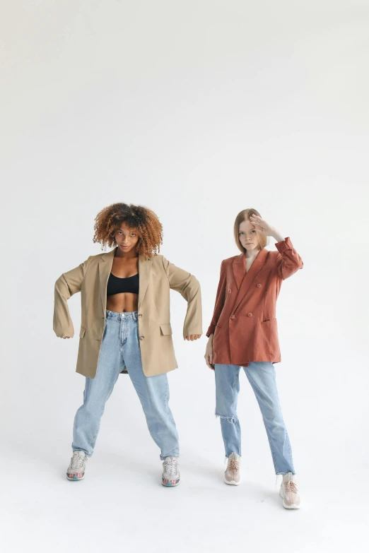 a couple of women standing next to each other, trending on pexels, choreographed, brown jacket, baggy jeans, on a pale background