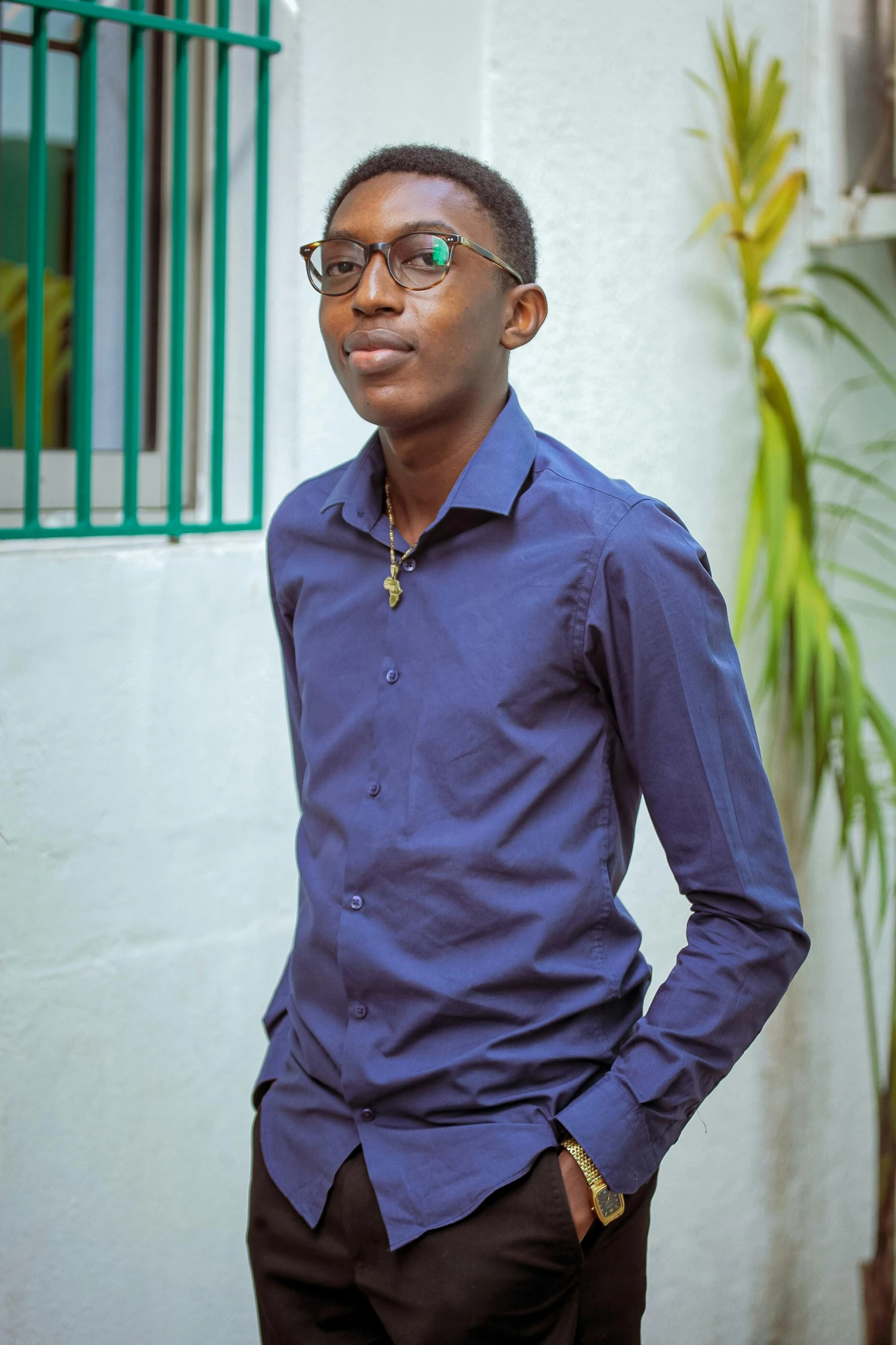 a man standing in front of a white building, an album cover, inspired by Ibram Lassaw, pexels contest winner, he wears a blue shirt, formal attire, black teenage boy, with glasses