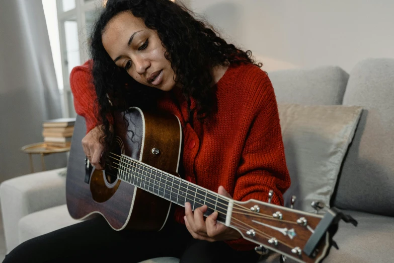 a woman sitting on a couch playing a guitar, by Winona Nelson, pexels contest winner, hurufiyya, mixed race, profile image, looking towards the camera, 38 years old