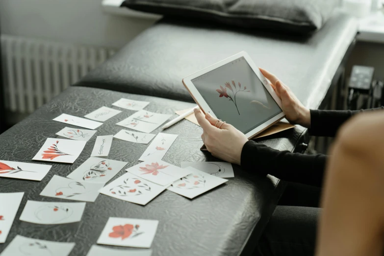 a woman sitting at a table using a tablet computer, a tattoo, by Adam Marczyński, trending on pexels, interactive art, throwing cards in the air, acupuncture treatment, flowery, puzzling