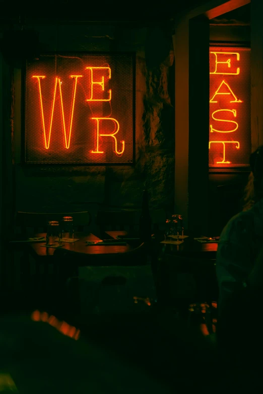 a person sitting at a table in front of a neon sign, by Lars Grant-West, unsplash contest winner, cozy dark 1920s speakeasy bar, the last day on earth, from east to west, scene from a dinner party