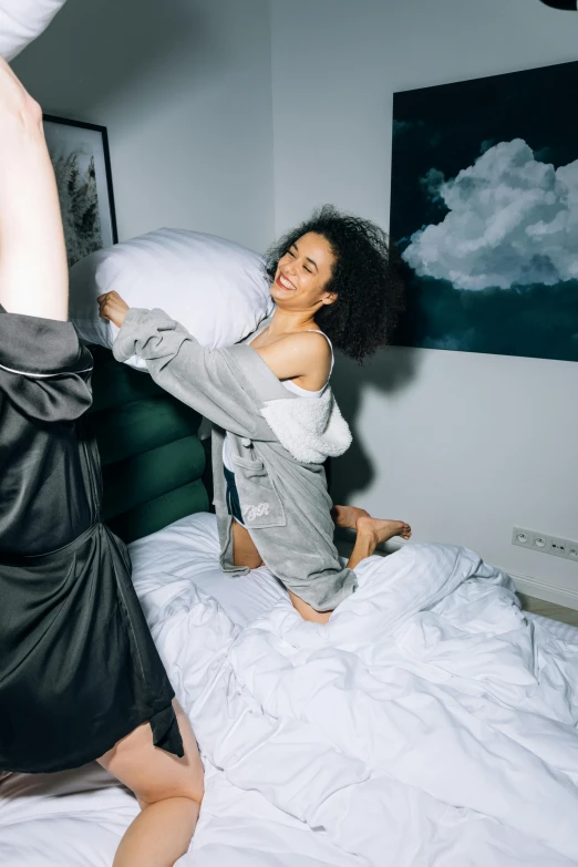 two women jumping in the air on a bed, inspired by Elsa Bleda, trending on pexels, happening, wearing a grey robe, doja cat, hungover, with afro