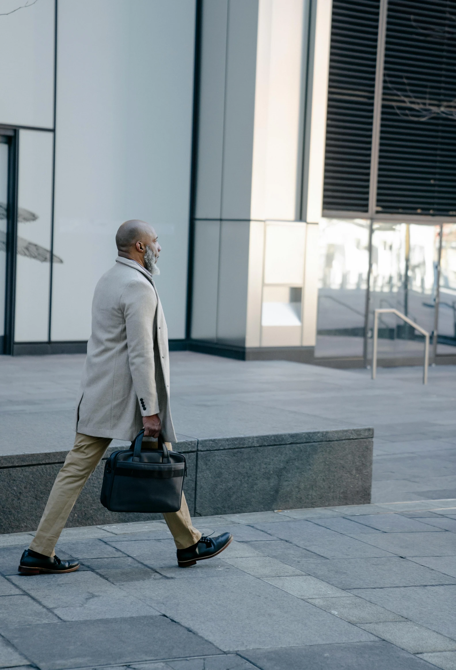 a man walking down a sidewalk carrying a briefcase, grey beard, jemal shabazz, without text, canary wharf