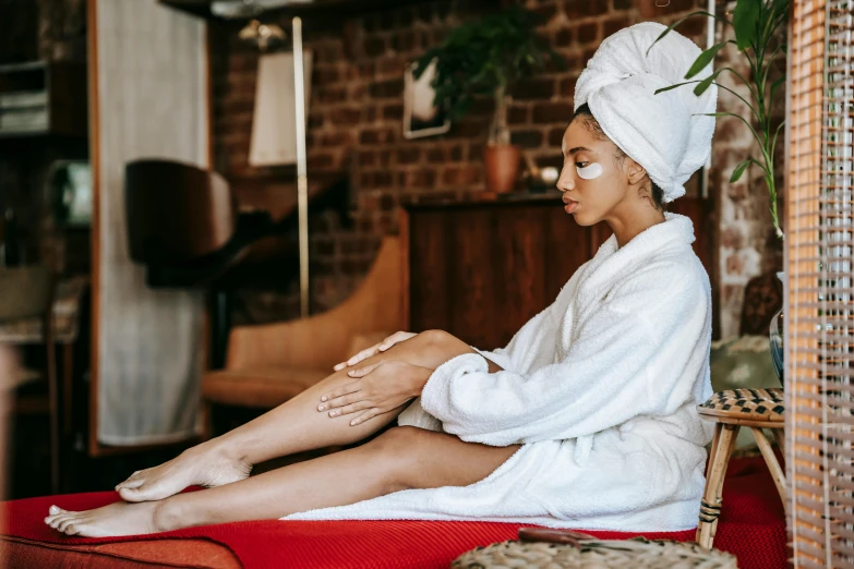 a woman sitting on a bed with a towel on her head, trending on pexels, sitting in a lounge, foot wraps, in a silk robe, manuka