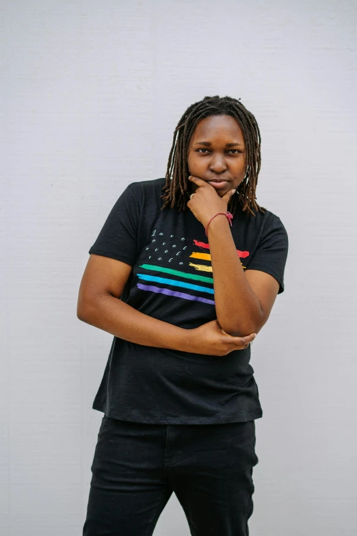 a woman standing in front of a white wall, unsplash, black arts movement, pride flag in background, he is wearing a black t-shirt, stars and stripes, official product image