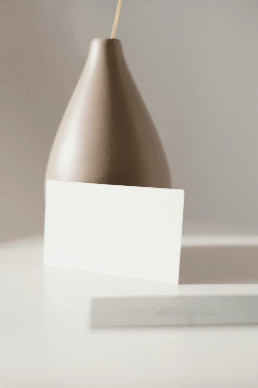 a brown vase sitting on top of a white table, unsplash, postminimalism, focus on card, dunce, white metallic, architectural