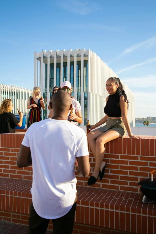 a group of people sitting on a brick wall, girl sitting on a rooftop, calarts, blue skies, college party