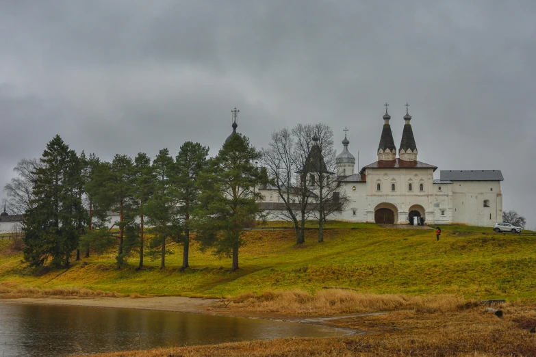 a church sitting on top of a hill next to a body of water, a portrait, inspired by Konstantin Vasilyev, pexels contest winner, renaissance, white wall complex, 000 — википедия, late autumn, grey