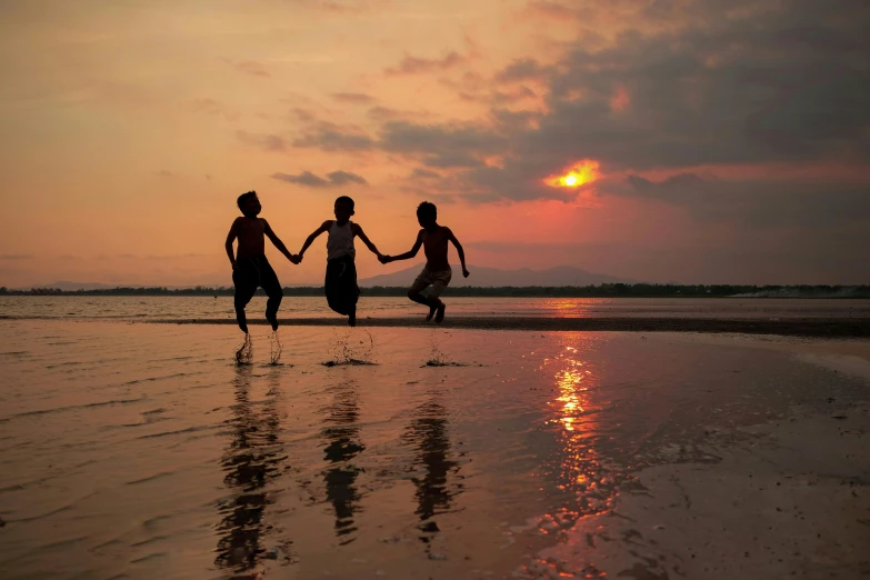 three people holding hands on a beach at sunset, by Jan Tengnagel, pexels contest winner, kids playing, indonesia, take off, dan mumfor