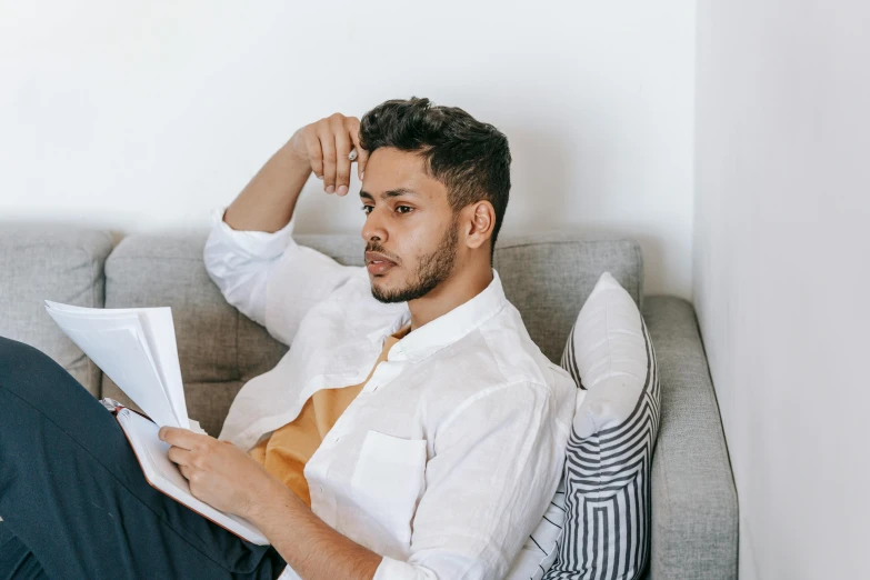 a man sitting on a couch reading a book, pexels contest winner, wearing a white shirt, thinking pose, a young man, ash thorp khyzyl saleem