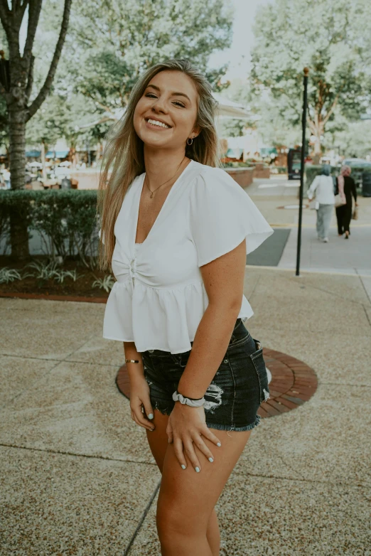 a woman standing on a sidewalk in a white top and black shorts, trending on unsplash, auburn outfit, at a mall, madly grinning, croptop