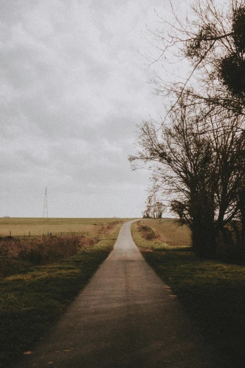 an empty road in the middle of a field, an album cover, by Jacob Toorenvliet, unsplash, multiple stories, overcast, pathway, near farm