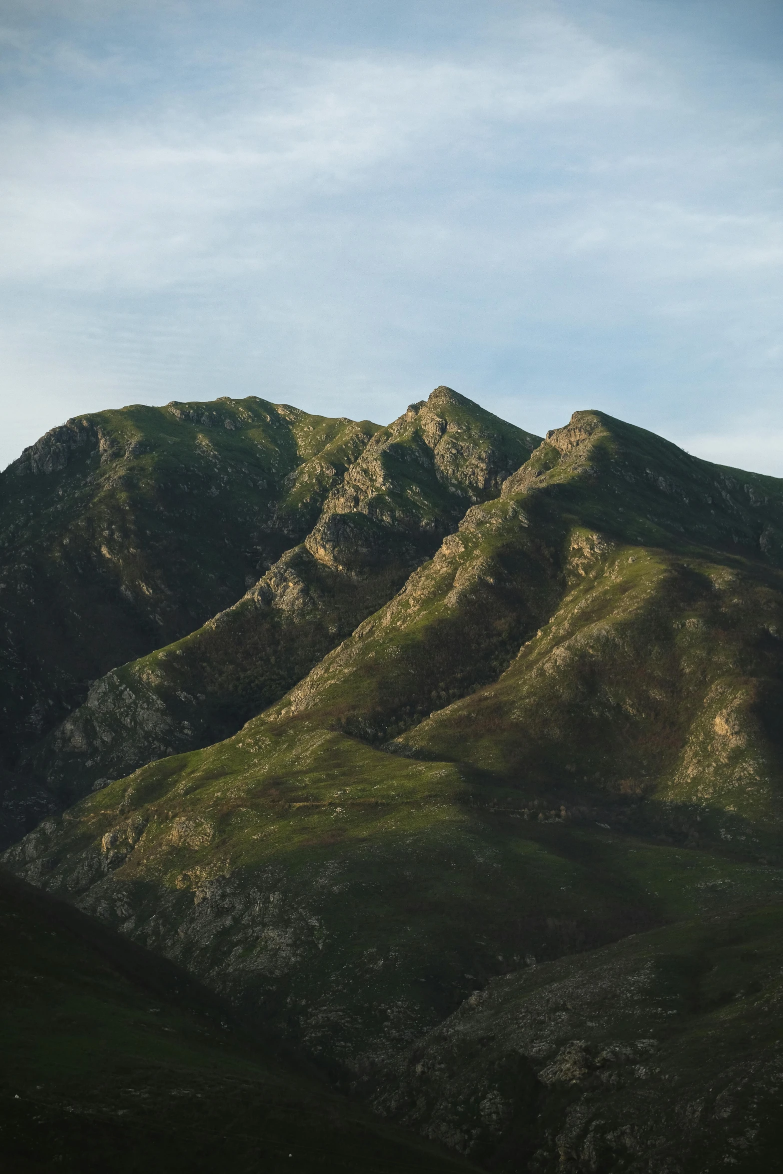 a couple of mountains sitting on top of a lush green hillside, last light on mountain top, chiseled features, zoomed out to show entire image, unsplash photography