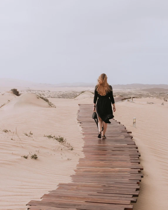 a woman walking on a boardwalk in the desert, pexels contest winner, south african coast, rain and thick strands of mucus, real trending on instagram image, victorian arcs of sand