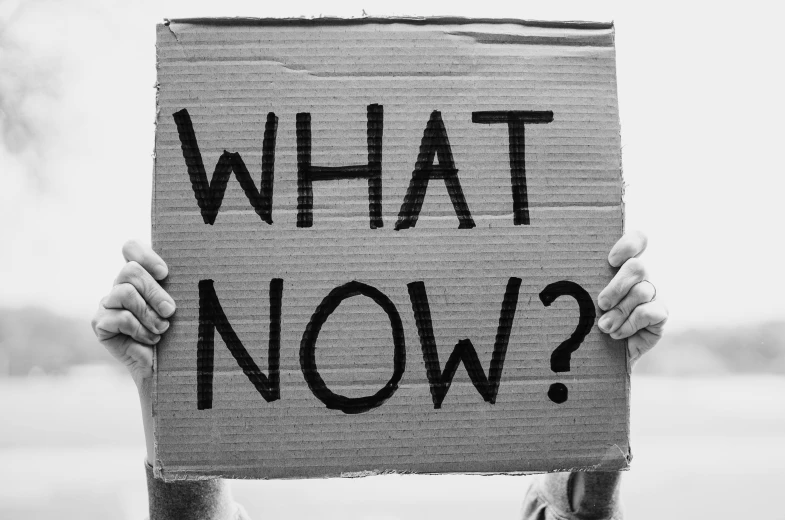 a person holding a sign that says what now?, a black and white photo, pixabay, happening, new album cover, cardboard, background image