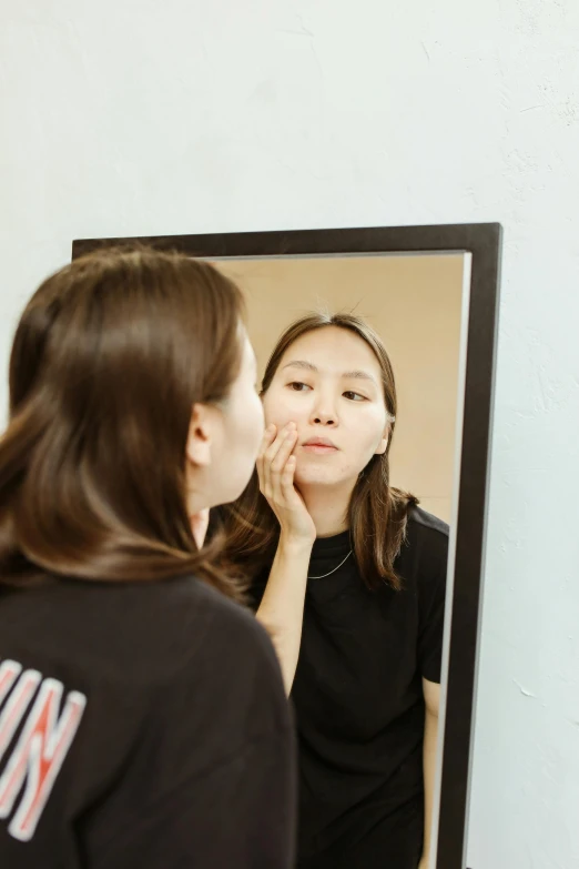 a woman standing in front of a mirror looking at her face, by Julia Pishtar, set on singaporean aesthetic, hand on cheek, cysts, square facial structure