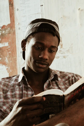 a man sitting in a chair reading a book, by Carey Morris, trending on unsplash, brown skinned, dressed in a worn, religious, headshot photo