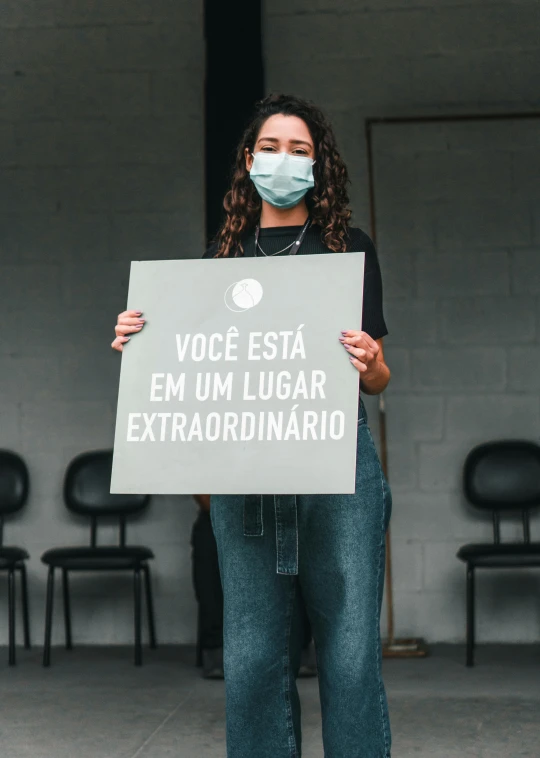a woman wearing a face mask holding a sign, by Olivia Peguero, pexels contest winner, excessivism, brazilian, wide full body, instagram post, profile picture