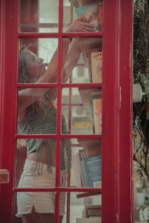 a woman standing in front of a red phone booth, a picture, happening, looking through a window frame, vhs footage still, bookshops, devon cady-lee