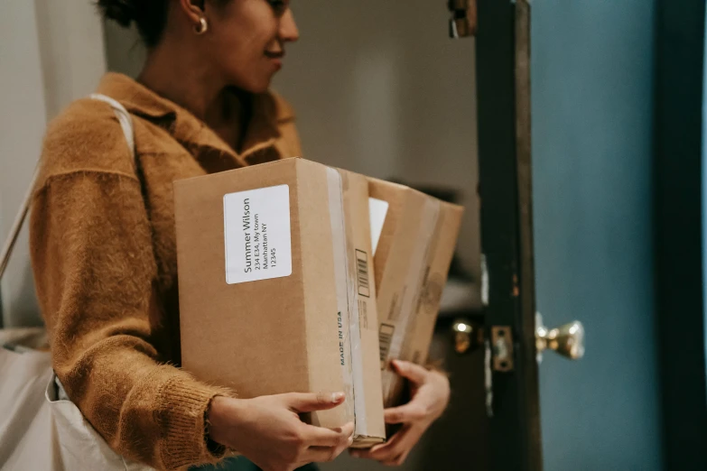 a woman holding a box in front of a door, pexels contest winner, private press, brown, packaging design, at checkout, multi-part