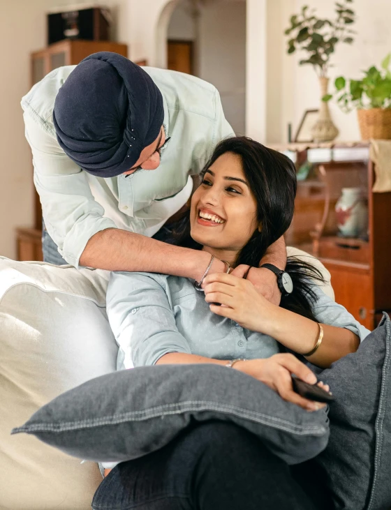 a woman sitting on top of a couch next to a man, inspired by Manjit Bawa, couple on bed, tight around neck, thumbnail, he also wears a grey beanie