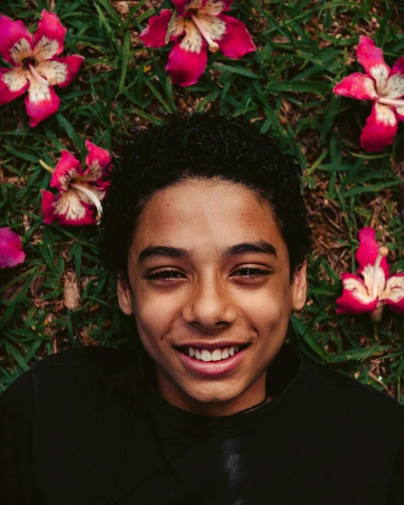 a young man laying on top of a lush green field of flowers, by Cosmo Alexander, trending on unsplash, black teenage boy, androgynous face, both smiling for the camera, on black background