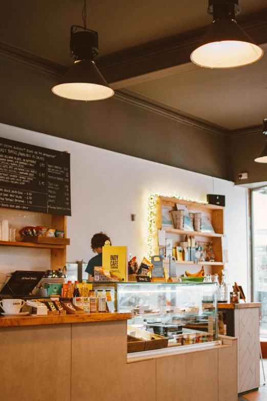 a person sitting at a table in front of a counter, trending on unsplash, cute bakery shop, lights on ceiling, thumbnail, aussie baristas