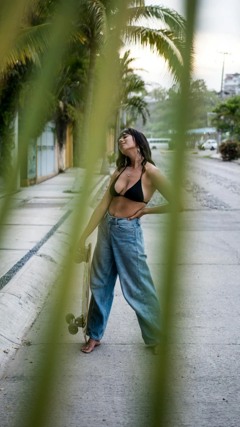 a woman walking down a street holding a skateboard, by Carey Morris, pexels contest winner, halter top, in the tropical wood, baggy jeans, alanis guillen