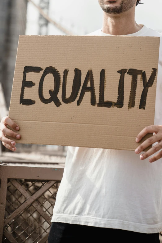 a man holding a sign that says equality, an album cover, trending on pexels, women, brown, square, celebration