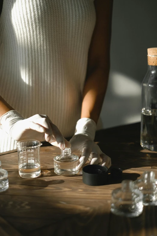 a woman in white gloves standing over a wooden table, trending on pexels, beakers full of liquid, plating, apothecary, opening shot