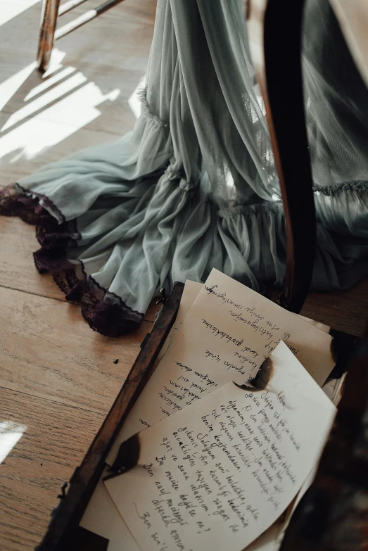 an open book sitting on top of a wooden table, by Sophie Pemberton, romanticism, tattered green dress, calligraphic poetry, pale cyan and grey fabric, editorial model