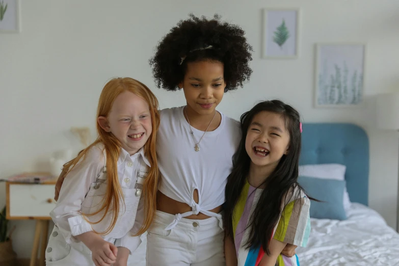 three girls standing next to each other on a bed, pexels contest winner, diverse ages, she is smiling, cute young redhead girl, mixed race