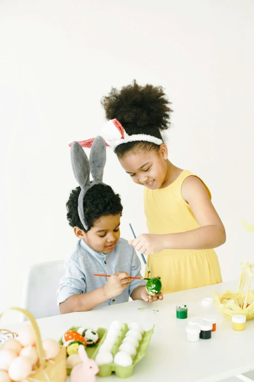 a couple of kids that are sitting at a table, wearing a headband, bunny, paint, product shot