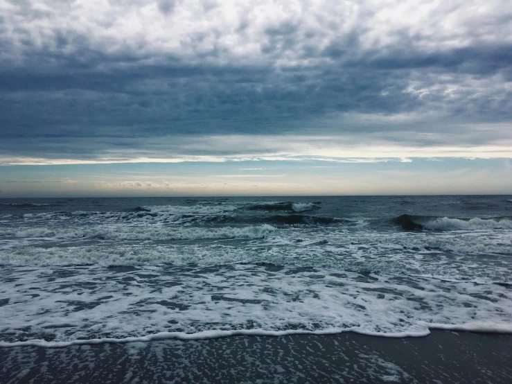 a large body of water sitting on top of a sandy beach, by Carey Morris, unsplash, stormy ocean, blue and grey, multiple stories, instagram picture