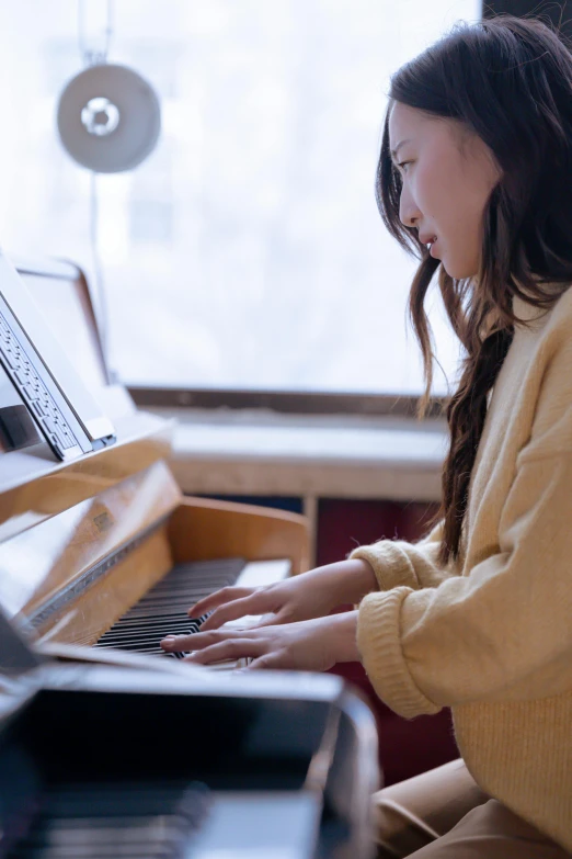 a woman sitting at a piano in front of a window, pexels contest winner, young asian girl, yellow, improvisational, mellotron