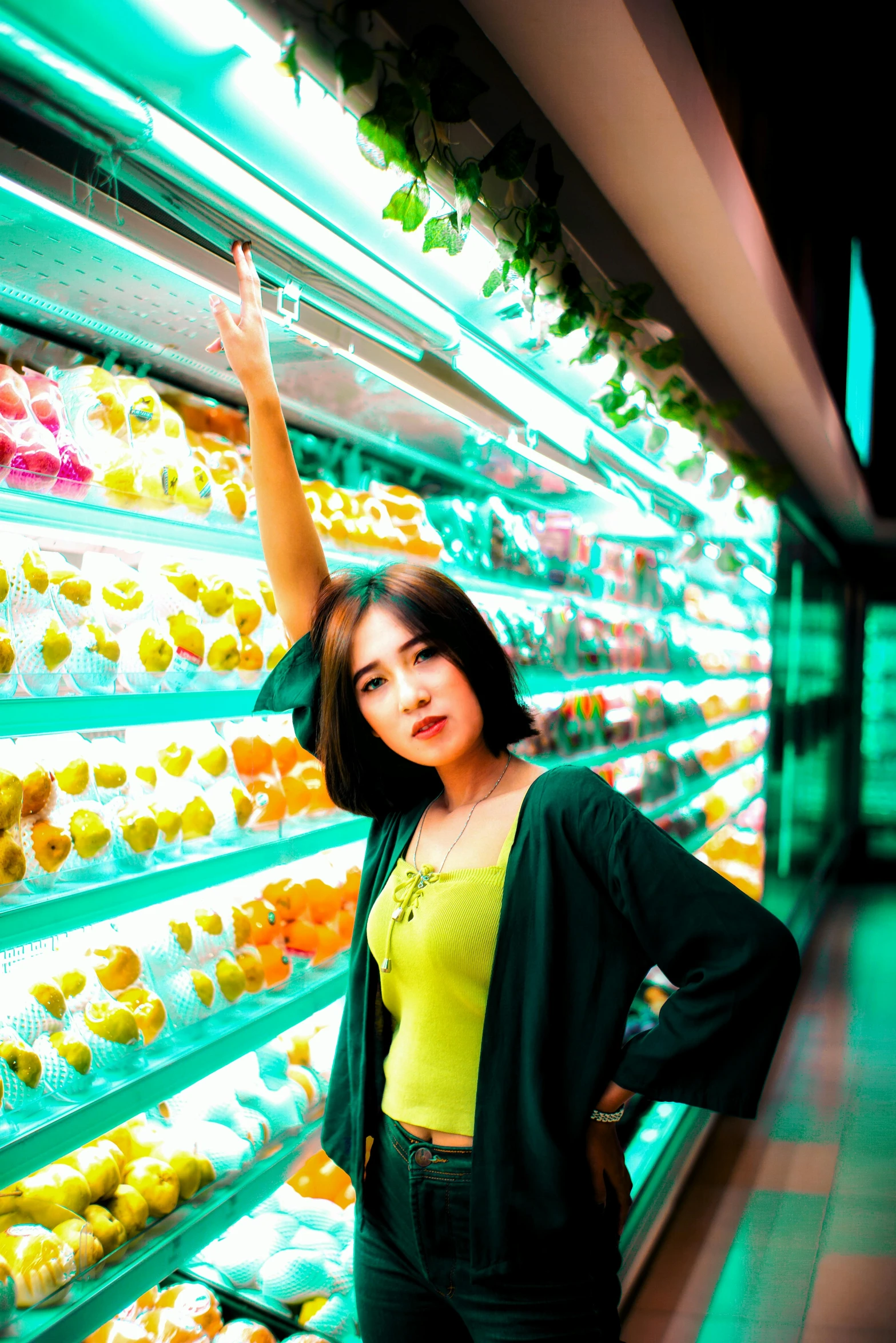 a woman standing in front of a display of fruit, inspired by Tan Ting-pho, unsplash, realism, hero pose colorful city lighting, stacking supermarket shelves, teal lights, selfie photo