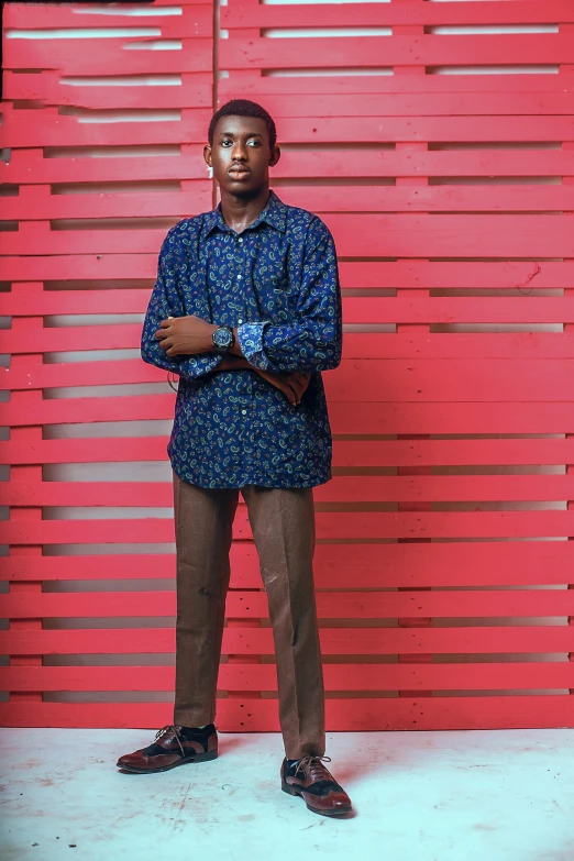 a man standing in front of a red wall, an album cover, by Chinwe Chukwuogo-Roy, 15081959 21121991 01012000 4k, patterned clothing, corporate photo, teenager