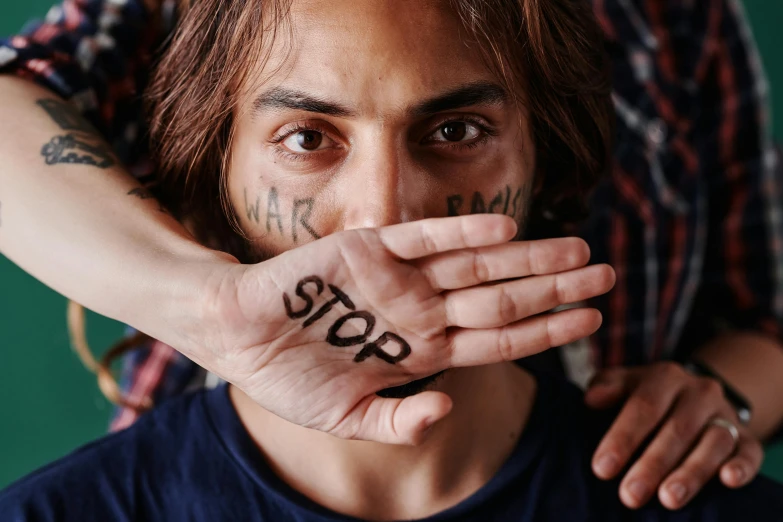 a man with a tattoo on his hand covering his mouth, trending on pexels, graffiti, avan jogia angel, stop sign, protest, striped