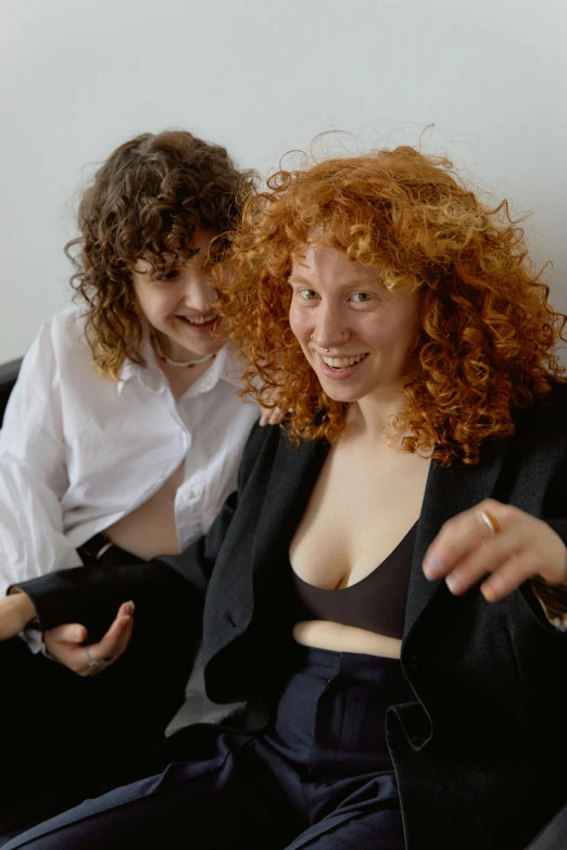 a couple of women sitting on top of a couch, inspired by Nan Goldin, unsplash, renaissance, with curly red hair, excited russians, loosely cropped, skintight suits