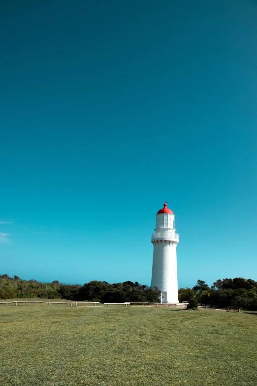 a white lighthouse sitting on top of a lush green field, melbourne, square, bright blue, single light