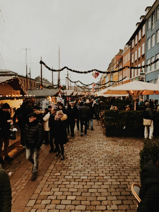 a crowd of people walking down a street next to tall buildings, by Jens Søndergaard, pexels contest winner, happening, fish market stalls, christmas, denmark, thumbnail