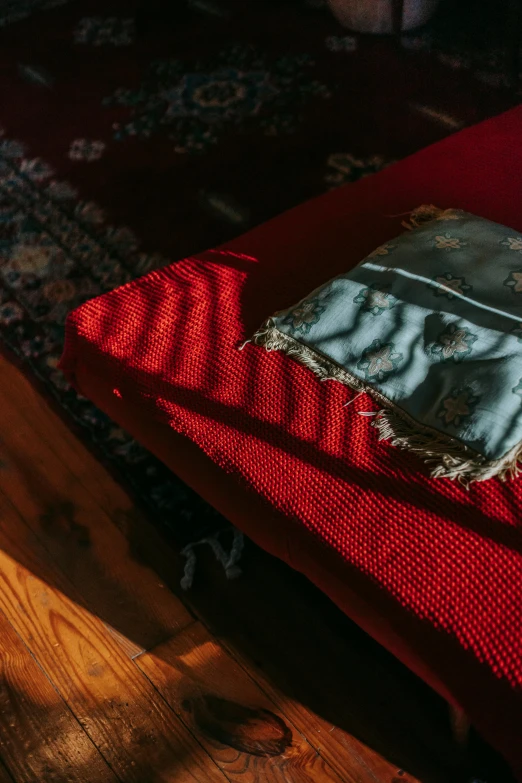 a red blanket sitting on top of a wooden floor, an album cover, inspired by Elsa Bleda, unsplash contest winner, visual art, aida muluneh, old couch, ignant, afternoon sunlight