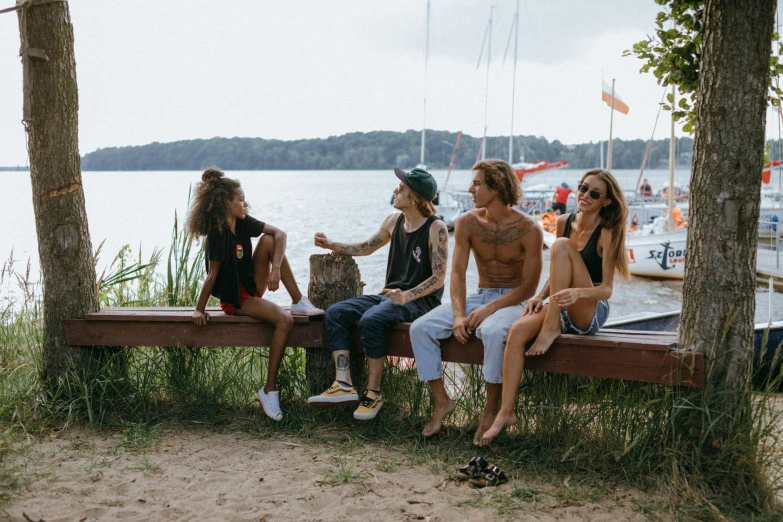 a group of people sitting on top of a wooden bench, pexels contest winner, wearing a tank top and shorts, federation clothing, lakeside, chillwave