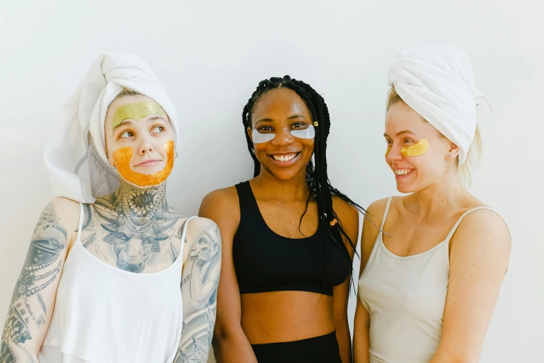 a group of three women standing next to each other, trending on pexels, spa, golden face tattoos, manuka, wearing a towel