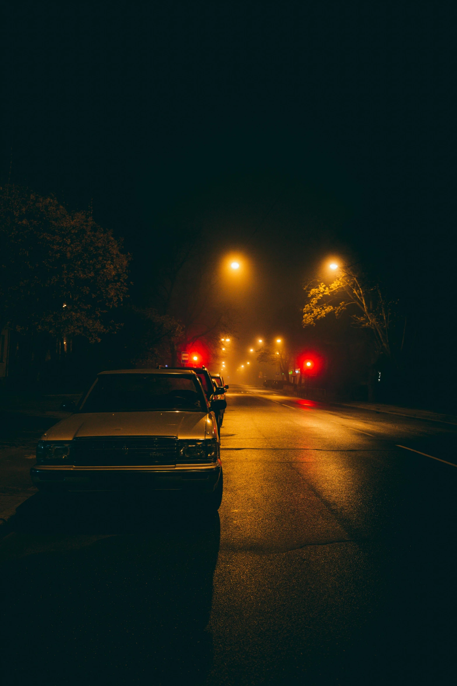 a car parked on the side of a road at night, inspired by Elsa Bleda, unsplash contest winner, realism, silent hill streets, kansas town at midnight, police car lights, orange fog